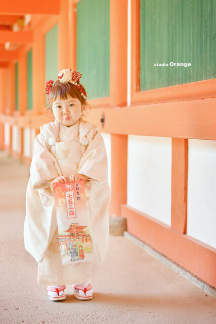 白い七五三着物を着た女の子が春日大社でもらった千歳飴を持っている