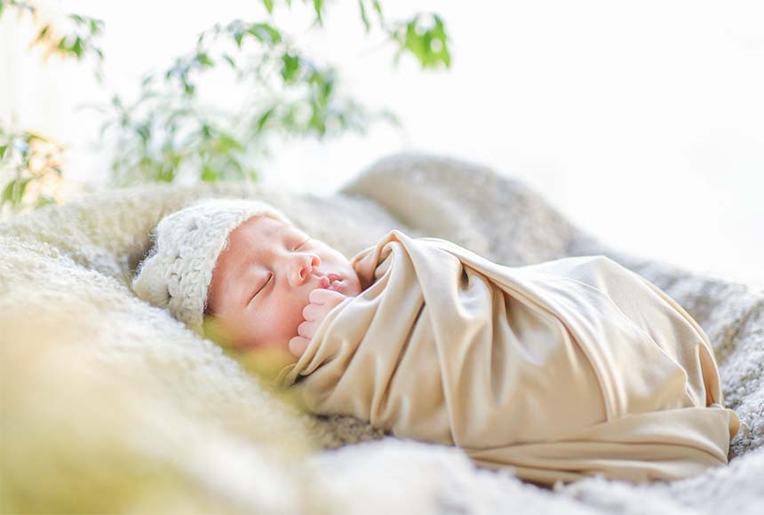 ベージュのおくるみに包まれて眠る新生児