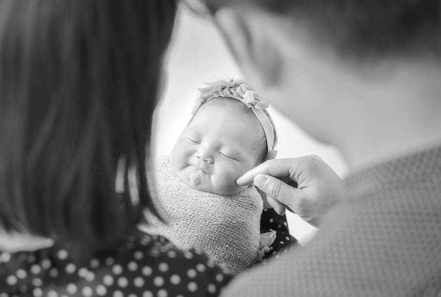 ママに抱っこしてもらい、パパにほっぺをツンツンされる新生児