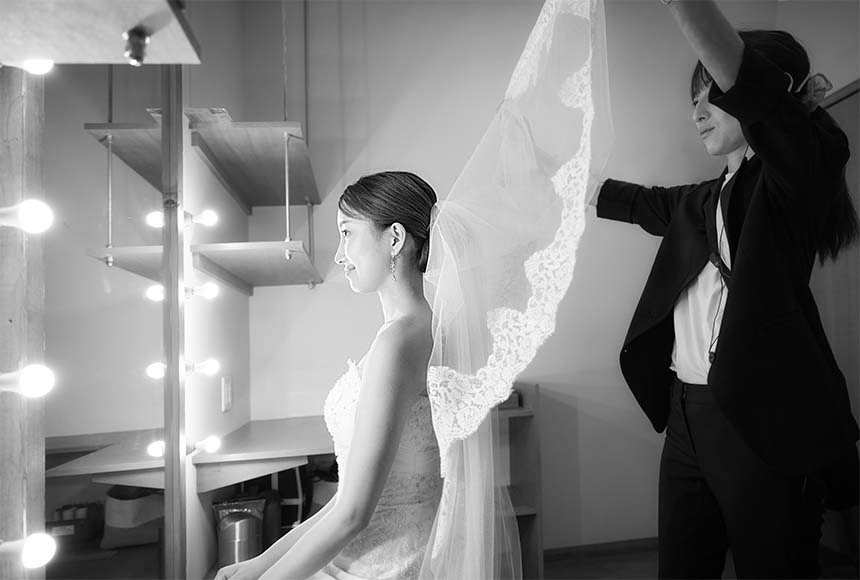 鏡の前に座り美容スタッフにベールをつけてもらう新婦