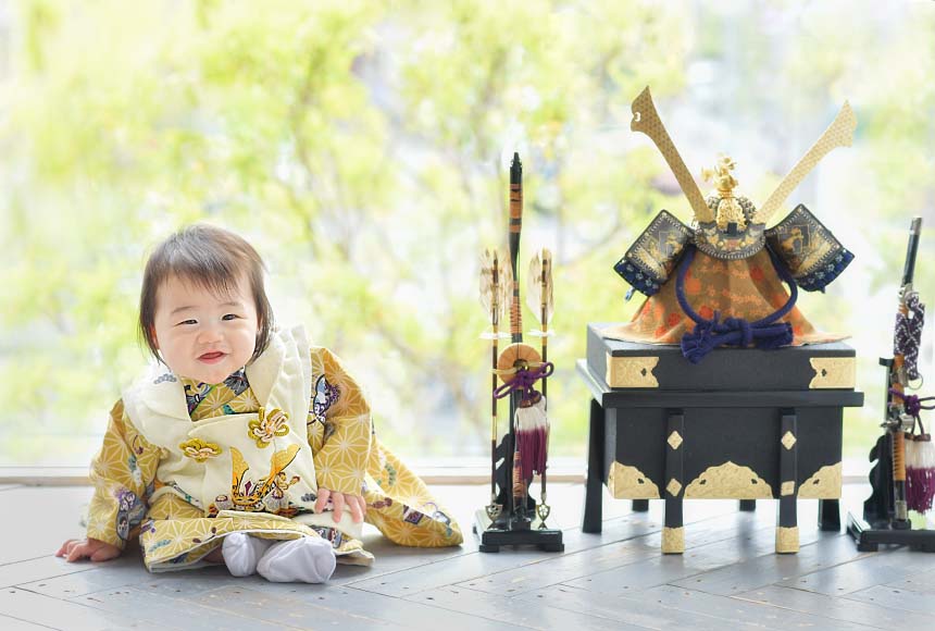 黄色の着物を着た男の子が兜と一緒に映った写真