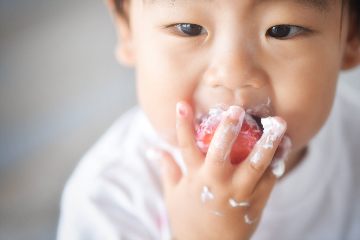 クリームだらけの手でイチゴを食べる男の子