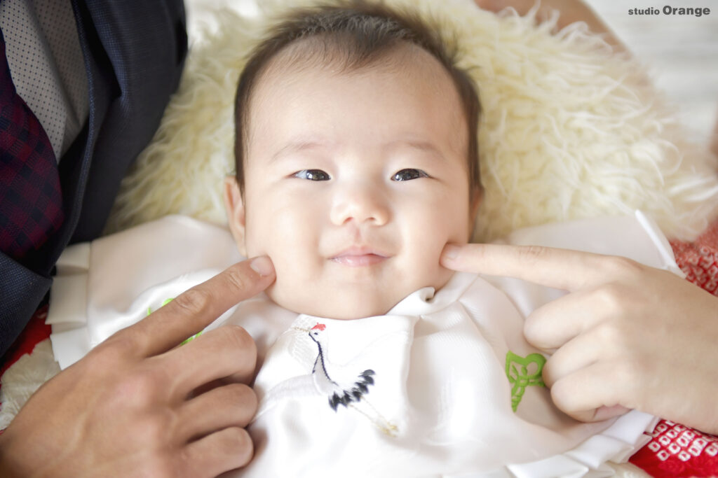 赤ちゃんがママとパパに指でほっぺを押されている写真