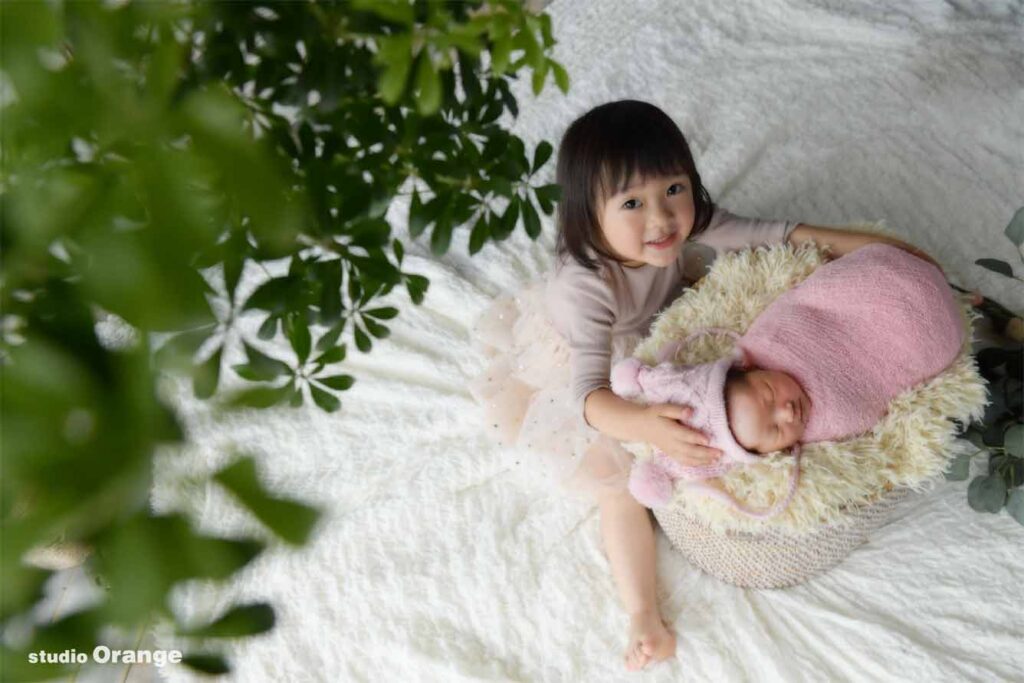 お姉ちゃんとおくるみにくるまっている妹のニューボーンフォト姉妹写真