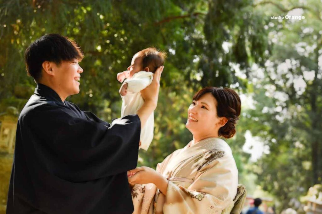 お宮参り出張撮影でパパにたかいたかいしてもらう女の子のあかちゃんと着物を着たお母さん