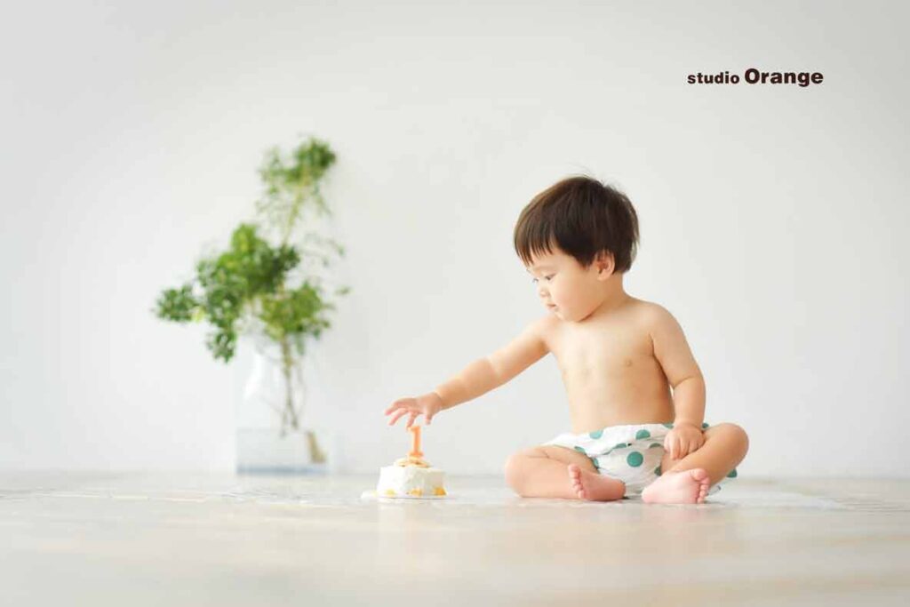 お誕生日撮影で1歳男の子がスマッシュケーキ に手を伸ばしている様子